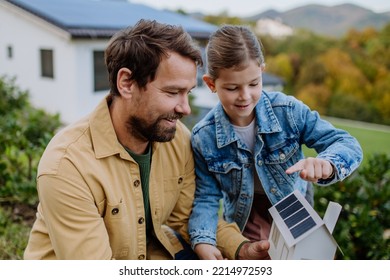 Little girl with her dad holding paper model of house with solar panels, explaining how it works.Alternative energy, saving resources and sustainable lifestyle concept. - Shutterstock ID 2214972593