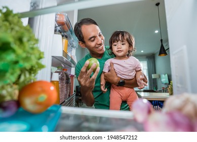 Little Girl And Her Dad Looking Inside The Fridge