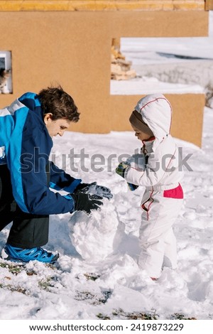 Little girl and her dad are making a snowman in the yard of a wooden house