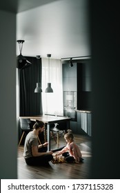 Little Girl And Her Father Play Chess At Home Sitting On The Floor. The Rays Of The Sun On The Floor. Scandinavian And Hi-tech Style In The Interior. Game Of Chess With Children. Family Leisure