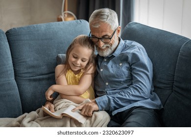 Little girl and her grandfather smiling as he reads her a book - Powered by Shutterstock