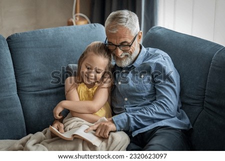 Little girl and her grandfather smiling as he reads her a book