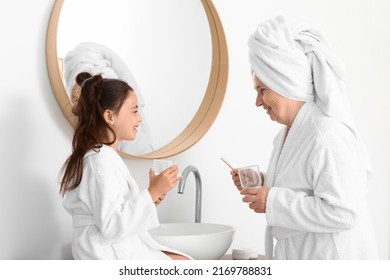 Little girl and her grandma with glasses of water in bathroom