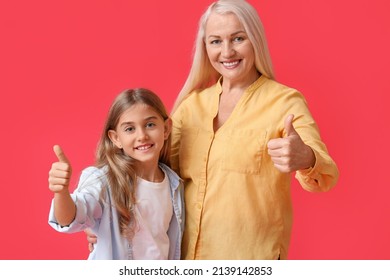 Little girl and her grandma showing thumbs-up on red background