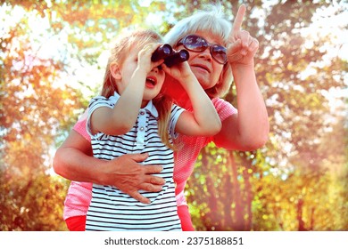 Little girl with her grandmother looking through binoculars outdoor. Discovery, adventure, having fun time with family. Birdwatching