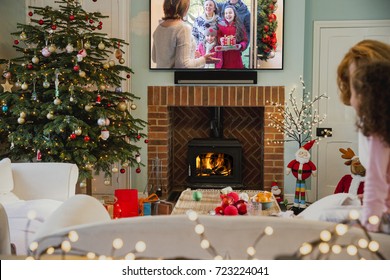 Little Girl And Her Grandmother Are Watching Festive Television Together At Home At Christmas Time.