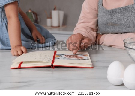 Little girl and her granny with recipe book in kitchen, closeup