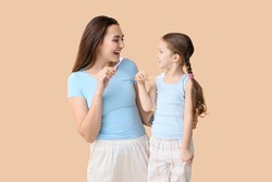 Little Girl With Her Mother Brushing Teeth On Beige Background