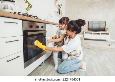 A little girl and her mother are cleaning the kitchen. a woman and a child wipe the oven in the kitchen. house cleaning. helping mom. - Powered by Shutterstock