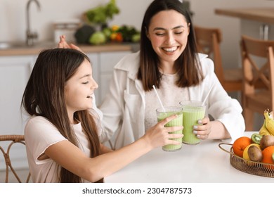 Little girl with her mother drinking green smoothie at table in kitchen - Powered by Shutterstock