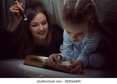 Kleines Mädchen und ihre Mutter lesen Märchen Buch unter den Decken am Abend mit Laterne. Kleines Kind spielen, bevor es schlafen geht, Bild tönt. Familienurlaub zu Hause.