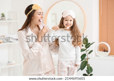 Little girl and her mother with sleeping masks brushing teeth in bathroom