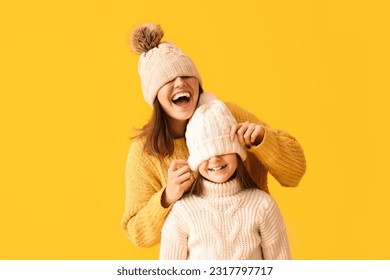 Little girl and her mother in warm hats and sweaters on yellow background - Powered by Shutterstock