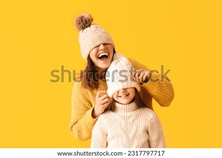Little girl and her mother in warm hats and sweaters on yellow background
