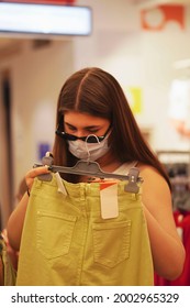     Little Girl And Her Older Sister In A Protective Medical Masks Choose School Uniform In A Store. Preparing For School. Prevention Of Coronavirus. Back To School Shopping.                     