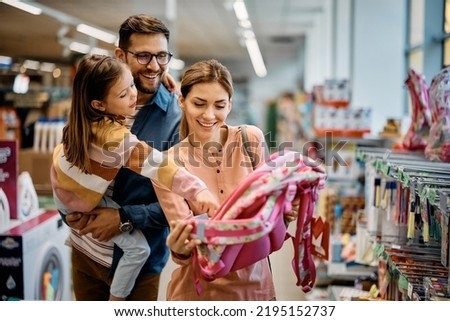 Little girl and her parents choosing backpack for school while shopping in the store together.
