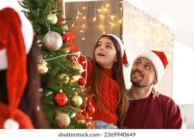 Little girl with her parents decorating Christmas tree at home