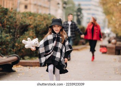 A little girl with her parents runs to the autumn city.A stylish family of three strolls through the autumn city - Shutterstock ID 2233923339