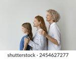 Little girl her young adult mummy and mature grandma posing on gray studio wall background, showing unity, deep-rooted connections, shared history among family members across different stages of life