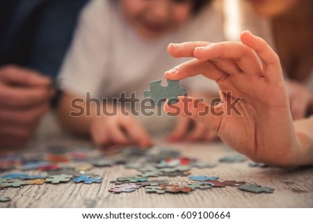 Little girl and her young parents are doing jigsaw puzzle while lying on the floor at home