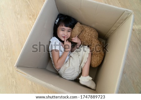 a little girl hide in cardboard box play hide and seek game having fun with parent in moving day to new house, asian family playful happy together concept.