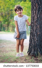 Little girl hiding behind a tree in the park.