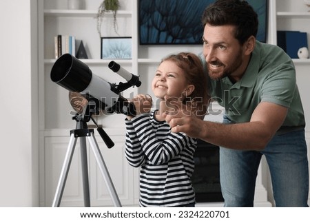 Little girl with his father looking at stars through telescope in room