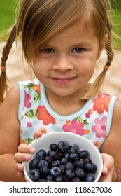 A little girl holding a dish of freshly picked blueberries