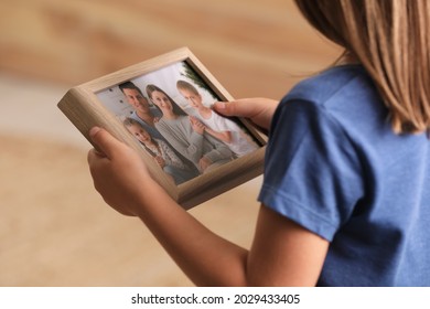 Little Girl Holding Framed Family Photo On Blurred Background, Closeup