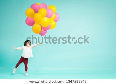 Little girl holding helium balloons on plain background