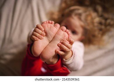 Little Girl Holding Her Legs Barefoot, Baby Feet Close-up In Focus. High Quality Photo