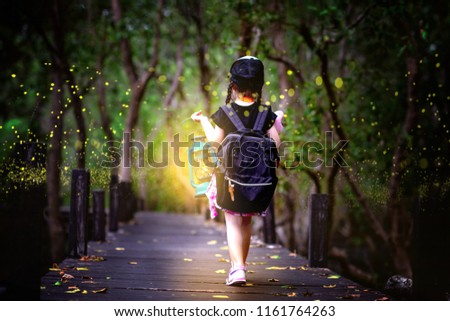 little girl holding lamp light walks on the wooden bridge in the forest of fen marsh see bundle of firefly in early dark of the night, field trip for a kids school learning the nature for kids school