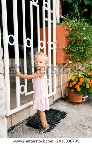 Little girl holding on to a metal gate near a stone fence