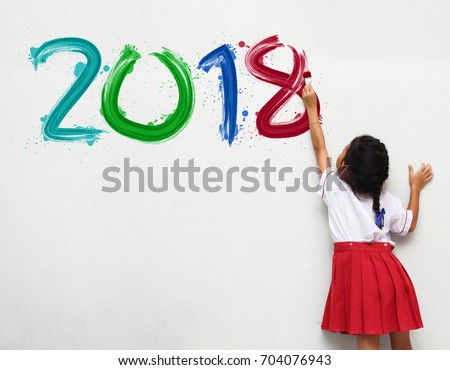 little girl holding a paint brush painting happy new year 2018 on a white wall background