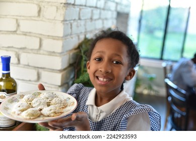 little girl holding a plate of freshly baked homemade cookies on Christmas, smiling big and happy with green Christmas garland draped in the background  - Powered by Shutterstock