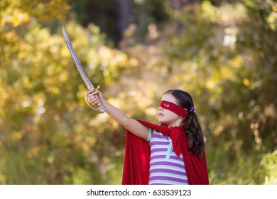 Little girl holding sword while wearing superhero costume in forest - Powered by Shutterstock