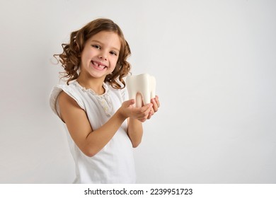 Little girl holding tooth on a white background with copy space. Portrait of happy girl with white teeth, close-up - Shutterstock ID 2239951723