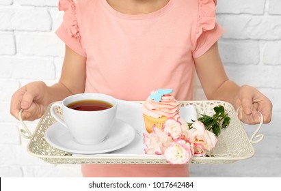 Little girl holding tray with breakfast and flowers for her mommy on Mother's Day against brick wall - Powered by Shutterstock