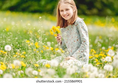Little girl holding yellow blowballs flowers in hands and sitting in blossom field smiling. Cute child kid with dandelions at nature