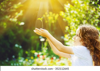 Little girl holding young green plant in sunlight. Ecology concept. Background toning to instagram filter. - Shutterstock ID 352112645