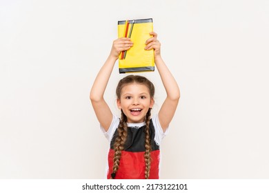 A little girl holds a book above her head on a white isolated background. Learning German in the lower grades. A child in a T-shirt with the flag of Germany.