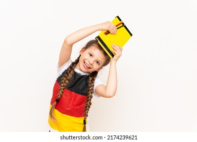 A little girl holds a book above her head on a white isolated background. Learning German in the lower grades. A child in a T-shirt with the flag of Germany.