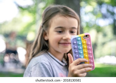 A little girl holds in her hand a phone in a case with pimples pop it, a trendy anti stress toy.