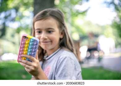 A little girl holds in her hand a phone in a case with pimples pop it, a trendy anti stress toy.