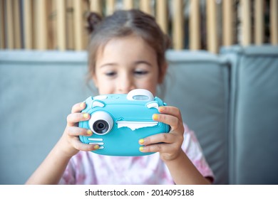 A Little Girl Holds In Her Hands A Blue Toy Digital Camera For Children For Instant Photo Printing.