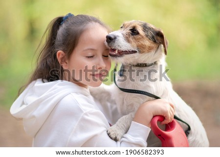 Little girl hugging her dog. Owner is walking with his pet in the park