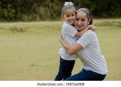 Little Girl Hugging Her Mom In The Park-young Hispanic Mom With Her Daughter Outdoors