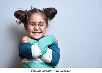 Little girl hugging herself and smiling isolated on white studio background. self love and self care concept