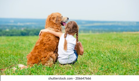 Little girl hugging retriever in the field, looking into the distance