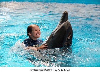 little girl hugging and swimming with bottlenose dolphins in blue water. Dolphin Assisted Therapy